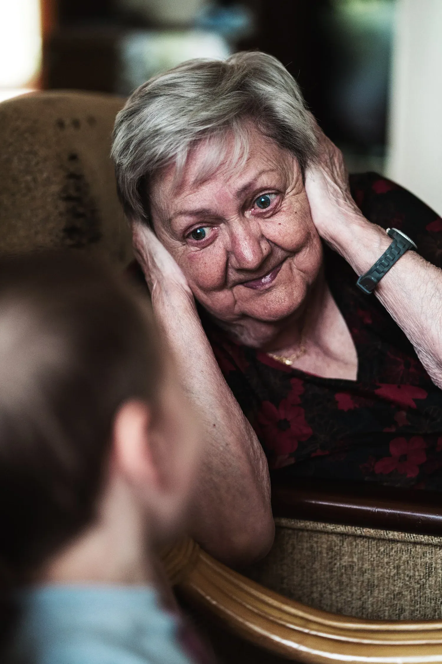 An older woman smiling with her hands on her cheeks, listening to a younger person