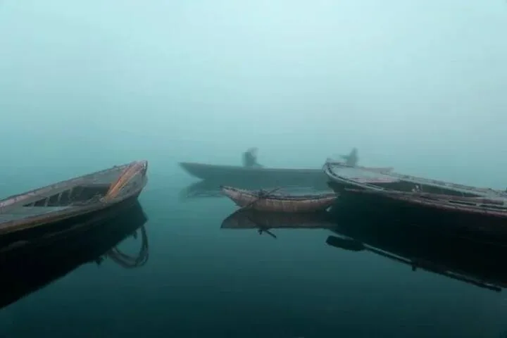 Two wooden boats on still water in morning fog