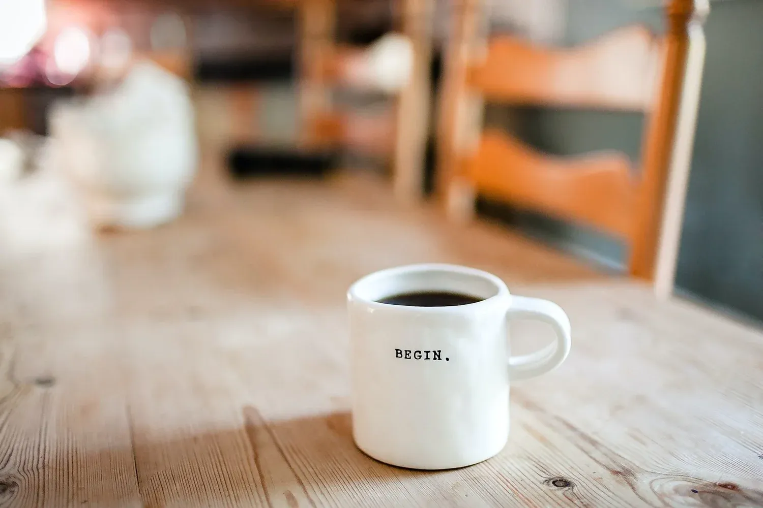 A white mug that reads Begin on a wooden table in soft morning light