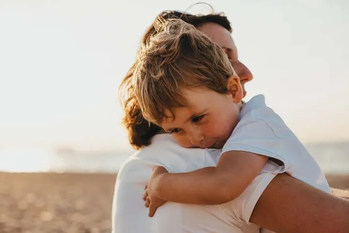A young child resting on a parent’s shoulder at the beach