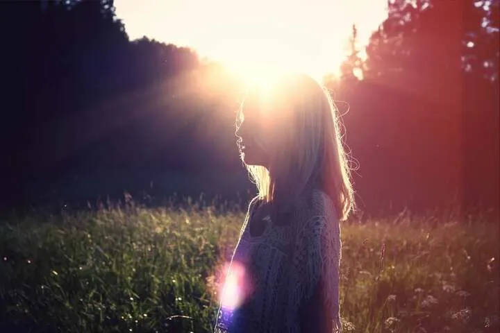 A person in a field at sunset, light flaring behind them
