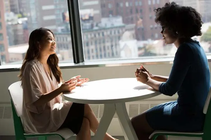 Two people talking across a small round table by a window